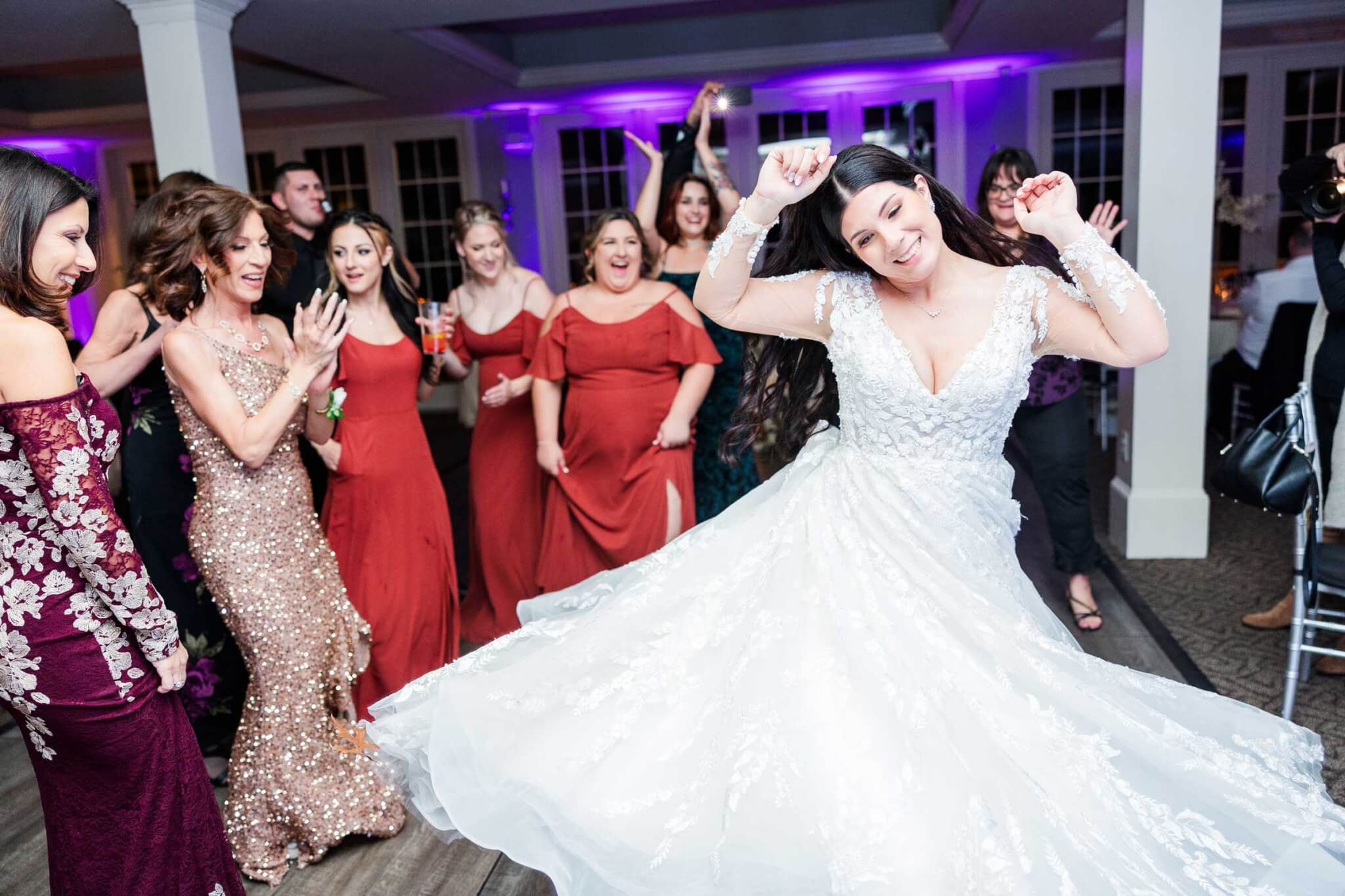 bride-dancing-at-her-wedding-sonic-djs A bride in a white dress dances energetically on the dance floor while guests in formal attire cheer and clap around her at a wedding reception.